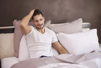 Homem sentado em uma cama coçando a cabeça após sonhar com piolho